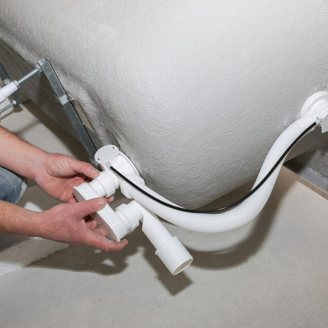 Bath installation. Worker is making drain with hose tube. Maintenance repair in the flat. Renovation process.