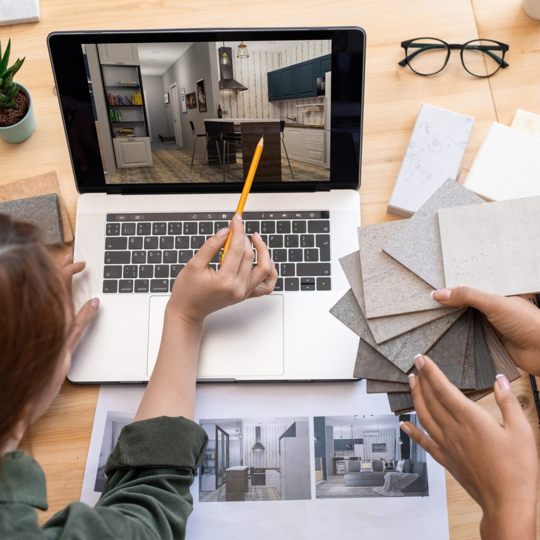 One of young women with pencil pointing at table in the picture of modern room on laptop display while discussing its design with colleague